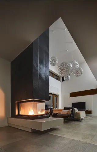 Ultra-modern living room with a striking floor-to-ceiling black slate fireplace and a three-sided glass firebox beneath a high, vaulted ceiling with contemporary spherical light fixtures.
